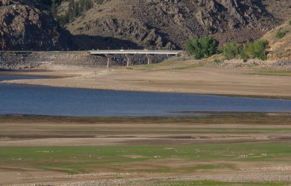 A concrete bridge spans over a river with low water levels, exposing wide areas of dry, grassy riverbed and rocky hills in the background.