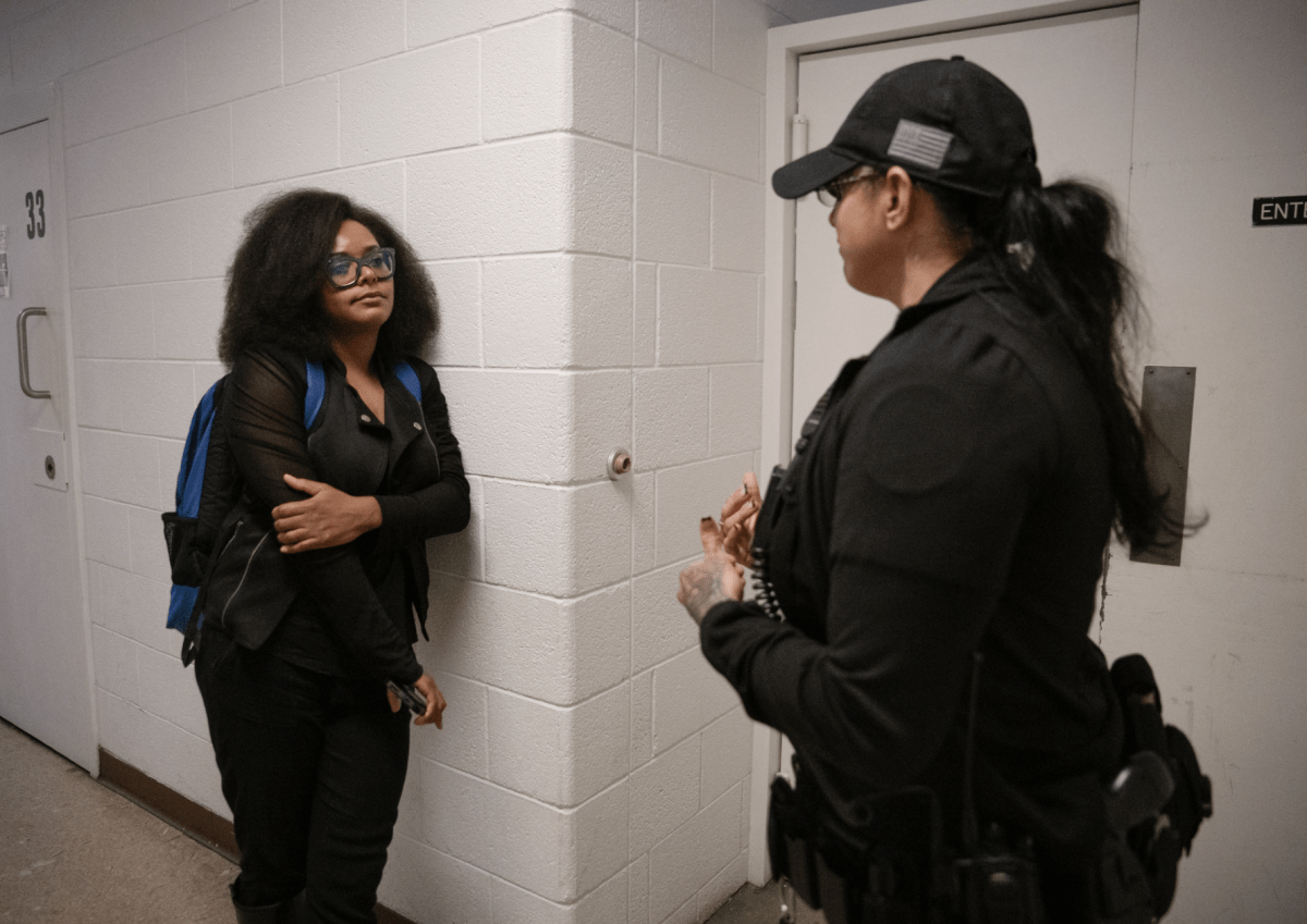 A woman leans against a wall while listening to a woman in uniform.